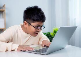 Educational of tech concept, Staying at home, Little Asian boy student using computer laptop learning. Presenting a modern educational way of life. Virtual internet online class from school teacher. photo