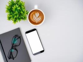 Top view of mock up modern workspace with blank screen smartphone, Coffee cup, Notebook, Pencil, Glasses. Office situation with keyboard and accessories isolated on white. Copy space, Flat lay. photo