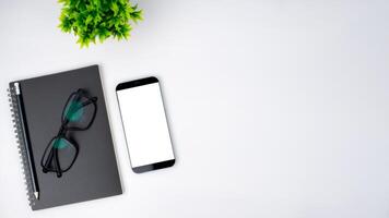 Top view of mock up modern workspace with blank screen smartphone, Coffee cup, Notebook, Pencil, Glasses. Office situation with keyboard and accessories isolated on white. Copy space, Flat lay. photo