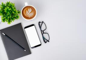 Top view of mock up modern workspace with blank screen smartphone, Coffee cup, Notebook, Pencil, Glasses. Office situation with keyboard and accessories isolated on white. Copy space, Flat lay. photo