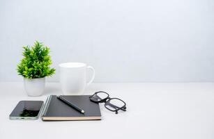 Workspace mock up white table top with vintage notebook, Pencils and green houseplant. Copy space desk with copy space for products display montage. Minimalist white workplace with supplies. photo