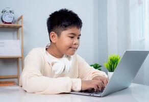 Educational of tech concept, Staying at home, Little Asian boy student using computer laptop learning. Presenting a modern educational way of life. Virtual internet online class from school teacher. photo