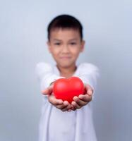 Portrait of Asian little boy child holding red heart sign on white background. photo