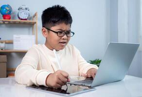 Little Asian boy student using computer laptop learning. Educational of tech concept, Staying at home, Presenting a modern educational way of life. Virtual internet online class from school teacher. photo
