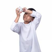 A boy wearing a white shirtis holding and trying to open a white piggy bank The concept of saving for the future. photo