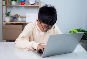 Educational of tech concept, Staying at home, Little Asian boy student using computer laptop learning, Presenting a modern educational way of life, Virtual internet online class from school teacher. photo