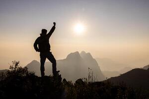 Climber success, silhouette achievements successful arm up man is on top of hill celebrating success with sunrise. photo