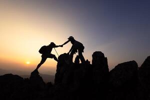 Two hikers helping each other climb a mountain at sunrise. Helping each other. Climbing. Rescue and teamwork concept. Helping hand in the mountains. photo