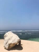 A large white stone positioned aesthetically on the white sand beach shore in Bali photo