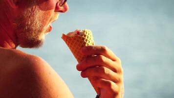 Man eating ice cream. Close-up portrait of young hipster man in sunglasses eating ice cream in summer hot weather on the beach, have fun and good mood. Travel, tourism, vacation, pleasure, enjoying. video