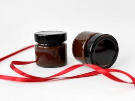 Elegant glass jars with chocolate spread with red ribbon on white background for gift packaging photo