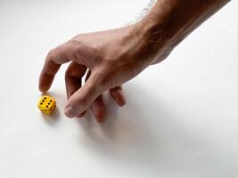 Hand reaching for yellow dice on white background symbolizing chance and decision-making photo