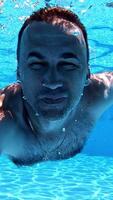 Man swimming underwater. Healthy man diving in the swimming pool and looking at camera. Happy male showing ok sign inside the pool. Vertical video