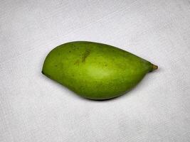 A vibrant green Totapuri mango with a smooth, oval shape and slightly curved stem. Small dark spots add texture to its surface, standing out against a neutral white background. photo