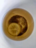 A top-down view of a paper cup filled with lemon tea, featuring a floating half-slice of lemon. Enjoyed for its refreshing taste, it offers a boost of vitamin C and potential health benefits. photo