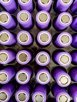 A closeup of neatly arranged cylindrical lithium-ion batteries in a vibrant purple with a metallic finish. Each battery displays clear positive terminals, creating a visually striking grid. photo