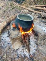 Traditional water heating with a stone-and-log charcoal stove and a large pot. The pot sits on burning charcoal, with vibrant flames heating the water, showcasing rustic simplicity and efficiency. photo