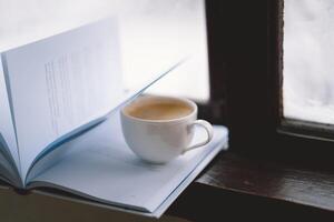 Cozy winter day with steaming coffee, open book, and candlelight by the snowy window photo