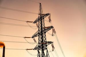 Tower of power lines on a background of orange sky. Transmission power, power tower on an empty farm land at the sunset photo