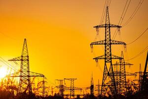 Transmission lines against the evening sky. High-voltage electric towers with wires on the setting sun background. Black pylons with electricity photo