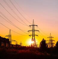 Transmission lines against the evening sky. High-voltage electric towers with wires on the setting sun background. Black pylons with electricity photo