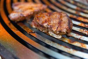 Juicy, seasoned meat steaks sizzle on a grill grate over burning coals, with flames and smoke rising as they cook to perfection. photo