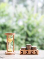 Hourglass, Wooden blocks with the number 2025 and stack of coins. The concept of saving money for manage time to success business in year 2025 photo