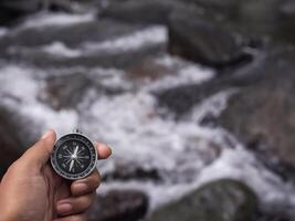 Close up of compass in woman hand with waterfall as background. The concept of world tourism day, Searching the right directions and Travel photo