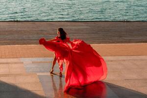 Sunrise red dress. A woman in a long red dress against the backdrop of sunrise, bright golden light of the sun's rays. The concept of femininity, harmony. photo