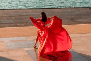 Sunrise red dress. A woman in a long red dress against the backdrop of sunrise, bright golden light of the sun's rays. The concept of femininity, harmony. photo