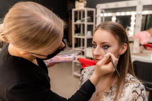 Make-up artist working with brush on model eyes Close up of applying make up on young girl,semi profile, professional make up in beauty studio photo