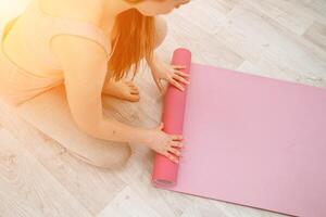 A young woman rolls a pink fitness or yoga mat before or after exercising, exercising at home in the living room or in a yoga studio. Healthy habits, keep fit, weight loss concept. Closeup photo