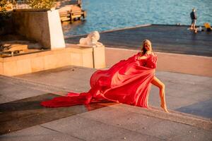 Sunrise red dress. A woman in a long red dress against the backdrop of sunrise, bright golden light of the sun's rays. The concept of femininity, harmony. photo