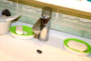 Chrome turned off faucet under shelf and part of bathroom sink, soap with shaving brush photo