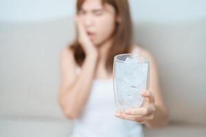 Teeth Sensitive to Cold concept. woman hold Ice Water glass and having toothache and pain after eat. Tooth Decay or Gum Disease, Grinding Teeth and Stress, Exposed Nerve Roots, Crack and Receding Gums photo