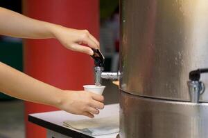 Turn on the Stainless-Steel cooler faucet. To add water to Conical paper cup to reduce the use of plastic which is difficult to decompose, the concept of energy conservation and save energy. photo