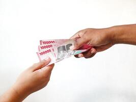 A man's hand gives Indonesian Rupiah money to a woman's hand with a nominal value of one hundred thousand rupiah. isolated background photo