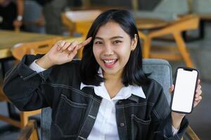 excited asian woman sitting in cafe showing smartphone empty screen and pointing finger to her head, think idea gesture photo