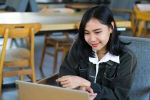 pretty asian woman using laptop in cafe doing virtual online meeting with client and watching course webinar with smile face photo