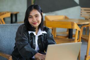 attractive and charming asian woman using laptop in cafe, typing and surfing in social media, smiling at camera photo