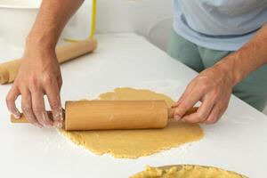 man rolling out dough with a rolling pin, making a pie at home photo