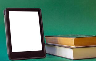 an electronic book next to a stack of paper books on a dark green background. one e-book replaces many regular books photo
