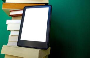 an electronic book next to a stack of paper books on a dark green background. one e-book replaces many regular books photo