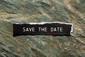 Save the date message written on ripped black torn paper piece with stone background. Conceptual save the date symbol. Copy space. photo