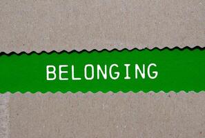 Belonging message written on ripped torn paper on green background. Conceptual belonging symbol. Copy space. photo