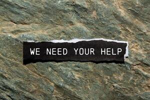 We need your help message written on ripped black torn paper piece with stone background. Conceptual we need your help symbol. Copy space. photo