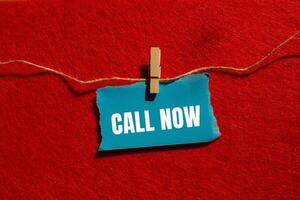 Call now message written on ripped torn blue paper piece with red background. Conceptual call now symbol. Copy space. photo