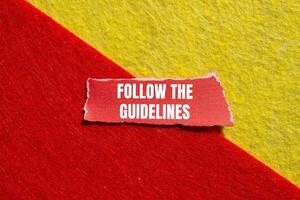 Follow the guidelines message written on ripped torn red paper piece with yellow red background. Conceptual follow the guidelines symbol. Copy space. photo