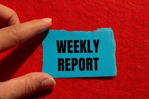 Weekly report message written on ripped torn blue paper piece with red background. Conceptual weekly report symbol. Copy space. photo