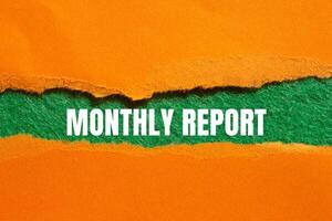 Monthly report message written on ripped torn orange paper with green background. Conceptual monthly report symbol. Copy space. photo